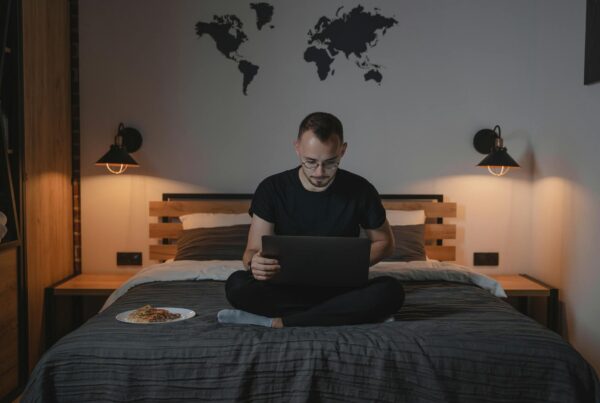 a man using a laptop while sitting on a bed