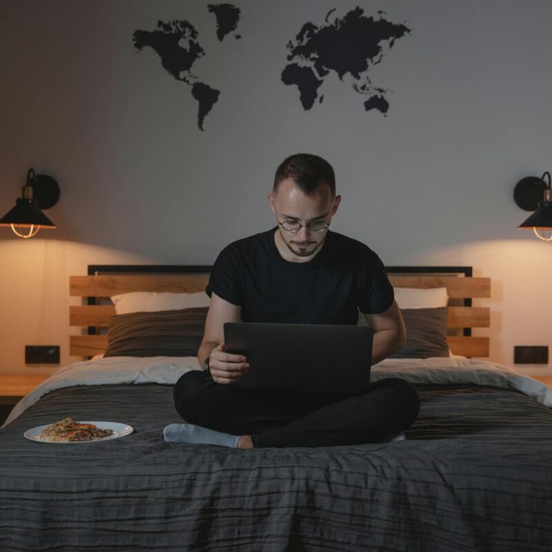 a man using a laptop while sitting on a bed
